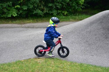 Mavi ceketli ve kasklı aktif bir genç açık hava pompa pistinde kırmızı denge bisikletine biniyor. Yeşil Park 'ta yaz günü bisiklet eğitimi alan bir çocuk. Aktif çocukluk ve spor kavramı.