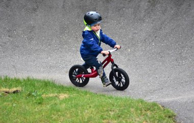 Mavi ceketli ve kasklı aktif bir genç açık hava pompa pistinde kırmızı denge bisikletine biniyor. Yeşil Park 'ta yaz günü bisiklet eğitimi alan bir çocuk. Aktif çocukluk ve spor kavramı.