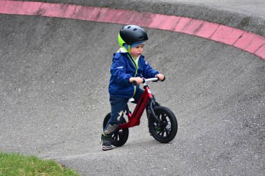 Mavi ceketli ve kasklı aktif bir genç açık hava pompa pistinde kırmızı denge bisikletine biniyor. Yeşil Park 'ta yaz günü bisiklet eğitimi alan bir çocuk. Aktif çocukluk ve spor kavramı.