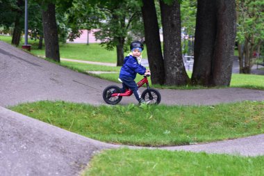 Mavi ceketli ve kasklı aktif bir genç açık hava pompa pistinde kırmızı denge bisikletine biniyor. Yeşil Park 'ta yaz günü bisiklet eğitimi alan bir çocuk. Aktif çocukluk ve spor kavramı.