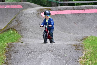 Mavi ceketli ve kasklı aktif bir genç açık hava pompa pistinde kırmızı denge bisikletine biniyor. Yeşil Park 'ta yaz günü bisiklet eğitimi alan bir çocuk. Aktif çocukluk ve spor kavramı.