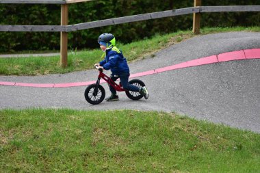 Mavi ceketli ve kasklı aktif bir genç açık hava pompa pistinde kırmızı denge bisikletine biniyor. Yeşil Park 'ta yaz günü bisiklet eğitimi alan bir çocuk. Aktif çocukluk ve spor kavramı.