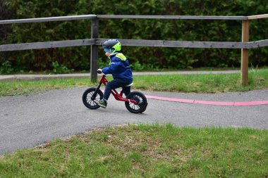 Mavi ceketli ve kasklı aktif bir genç açık hava pompa pistinde kırmızı denge bisikletine biniyor. Yeşil Park 'ta yaz günü bisiklet eğitimi alan bir çocuk. Aktif çocukluk ve spor kavramı.