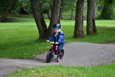 Mavi ceketli ve kasklı aktif bir genç açık hava pompa pistinde kırmızı denge bisikletine biniyor. Yeşil Park 'ta yaz günü bisiklet eğitimi alan bir çocuk. Aktif çocukluk ve spor kavramı.