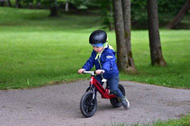 Mavi ceketli ve kasklı aktif bir genç açık hava pompa pistinde kırmızı denge bisikletine biniyor. Yeşil Park 'ta yaz günü bisiklet eğitimi alan bir çocuk. Aktif çocukluk ve spor kavramı.