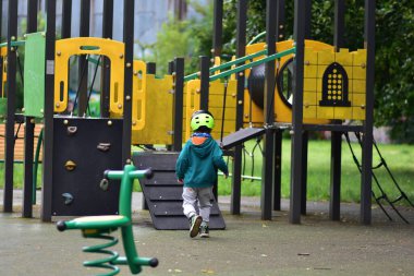 Kasklı genç bulutlu bir günde renkli oyun alanına yaklaşıyor. Çocuk maceraya ve aktif oyuna hazır, güvenliği, keşfi ve şehir parkında motor becerileri geliştirmeyi vurguluyor.