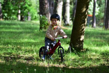 Güneşli orman parkında kasklı bisiklete binen genç bir çocuk. Sabit duruyor, geleceğe bakıyor, açık havada geçen çocukluk zamanlarında macerayı, odaklanmayı ve doğayla olan bağlantıyı simgeliyor..