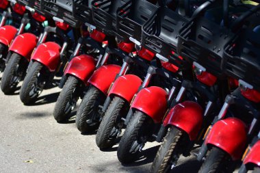 Yakın plan kırmızı kiralık e-scooter 'lar asfalta park edilmiş. Kentsel hareketlilik kavramını canlı renklerle ve tekrarlanan kalıplarla paylaştık. Modern eko taşıma çözümü.