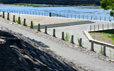 Asfalt kaldırımlı, basamaklı ve parmaklıklı modern nehir kenarı geçidi. Huzurlu kamusal alan su kenarında rahatlama, yürüme ve manzaralı manzaralar için kentsel tasarım içerir..