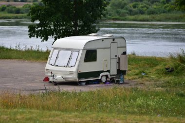 Sakin bir nehrin kenarına park edilmiş eski model bir karavan. Basit bir yaz kampı sahnesi, doğa geçmişi ve bazı açık hava aksesuarları..