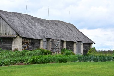 Yeşil sebze bahçesiyle çevrili, eğimli çatılı eski ahşap ve tuğla ahır. Geleneksel kırsal tarım manzarası.