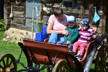 Büyükannem iki çocuğuyla bir kulübeye yakın, ahşap bir arabada oturuyor. Açık havada, aile içinde sevgi, bağ ve kuşak bağıyla geçen yaz..