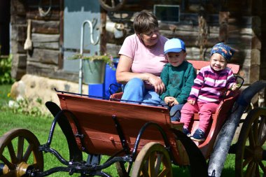 Büyükannem iki çocuğuyla bir kulübeye yakın, ahşap bir arabada oturuyor. Açık havada, aile içinde sevgi, bağ ve kuşak bağıyla geçen yaz..
