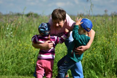 Büyük anne, çiçek açan bir yaz tarlasında iki çocuğu kucaklıyor. Sıcak aile anı, gün ışığında çekildi. Aşkı, bağı ve dışarıdaki bağları sembolize ediyor..