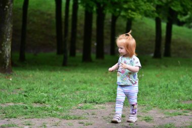 Kızıl saçlı çocuk elinde küçük bir sopayla oyun parkının yanındaki çimenlik yolda yürüyor..