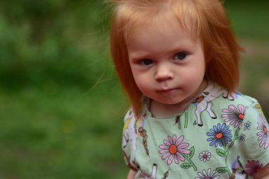 Parkta tek boynuzlu at tişörtlü kızıl saçlı bir çocuğun yakın plan portresi. Meraklı ve düşünceli yüz ifadesi..