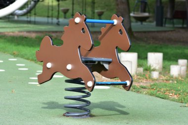 Yeşil güvenlik yüzeyi üzerinde oyun parkında boş kahverengi at binicisi, güneşli bir gün, bulanık park arka planı, çocuklar eğlence ve eğlence için açık hava oyun ekipmanları.