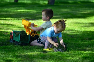 Oyuncak kamyonlar ve çimenlikte çimlerle dolu sepetlerle oynayan iki çocuk. Yaz günü eğlencesi, yaratıcı oyun, takım çalışması ve doğadaki çocukluk sevinci..