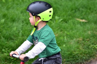 Yeşil tişörtlü ve kasklı bir çocuğun parkta kırmızı dengeli bisiklet sürüşünün, açık hava aktivitesinin, denge eğitiminin, sağlıklı çocukluk yaşam tarzının ve bisiklet geliştirmenin tadını çıkarışının yan görüntüsü..