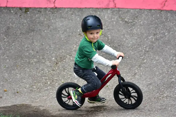Kask takan küçük çocuk asfalt tulumba pistinde kırmızı dengeli bisiklet sürüyor. Aktif çocuk parkta oynarken denge ve koordinasyon öğreniyor.