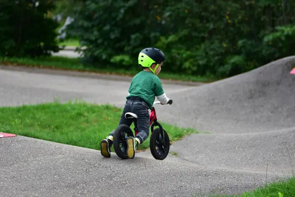 Kask takan küçük çocuk asfalt tulumba pistinde kırmızı dengeli bisiklet sürüyor. Aktif çocuk parkta oynarken denge ve koordinasyon öğreniyor.
