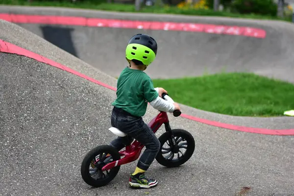 Kask takan küçük çocuk asfalt tulumba pistinde kırmızı dengeli bisiklet sürüyor. Aktif çocuk parkta oynarken denge ve koordinasyon öğreniyor.