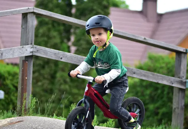 Kask takan küçük çocuk asfalt tulumba pistinde kırmızı dengeli bisiklet sürüyor. Aktif çocuk parkta oynarken denge ve koordinasyon öğreniyor.