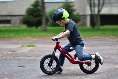 Energetic little boy riding red balance bike on asphalt, wearing safety helmet. Child in motion enjoying speed and outdoor fun activity. Childhood playtime concept.