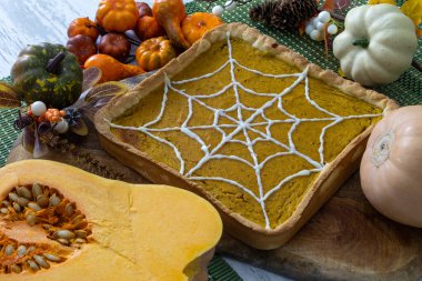 Örümcek ağı dizaynlı balkabağı turtası, balkabağı, yaprak ve kozalak süslemeleri ile çevrili.