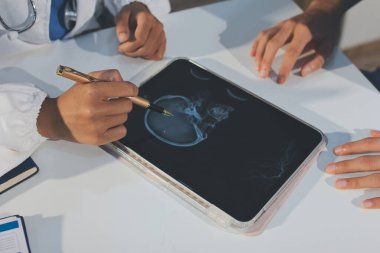 Tanımlanamayan bir doktorun hastasıyla oturup röntgenlerini dijital tablette gösterirken görüntüsü kesilmiş.