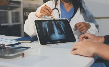 Tanımlanamayan bir doktorun hastasıyla oturup röntgenlerini dijital tablette gösterirken görüntüsü kesilmiş.