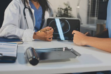 Tanımlanamayan bir doktorun hastasıyla oturup röntgenlerini dijital tablette gösterirken görüntüsü kesilmiş.