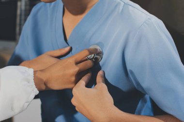 Bir doktor klinik randevusu sırasında hastanın kalbini incelemek için steteskop kullanır..