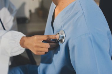 Bir doktor klinik randevusu sırasında hastanın kalbini incelemek için steteskop kullanır..