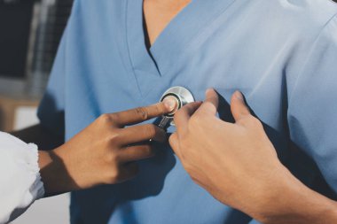 Bir doktor klinik randevusu sırasında hastanın kalbini incelemek için steteskop kullanır..