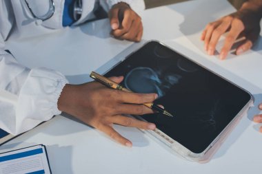 Tanımlanamayan bir doktorun hastasıyla oturup röntgenlerini dijital tablette gösterirken görüntüsü kesilmiş.