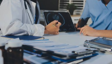 Tanımlanamayan bir doktorun hastasıyla oturup röntgenlerini dijital tablette gösterirken görüntüsü kesilmiş.