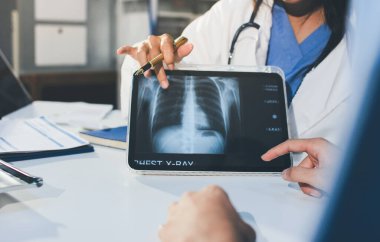 Tanımlanamayan bir doktorun hastasıyla oturup röntgenlerini dijital tablette gösterirken görüntüsü kesilmiş.