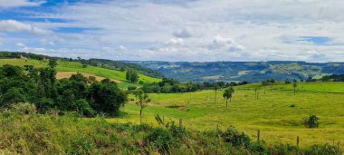 Sabahları yeşil çimenler ve bulutlarla dolu açık bir arazinin manzarası..