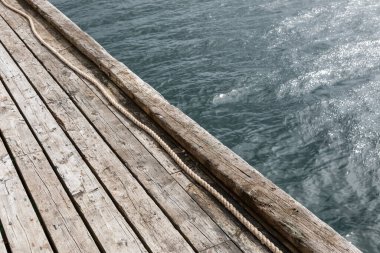 Norveç 'te fiyortlu ahşap iskele. Yıpranmış kalaslar ve berrak sudaki hafif dalgalar bu İskandinav kıyı sahnesinde sakin bir deniz atmosferi yaratır..