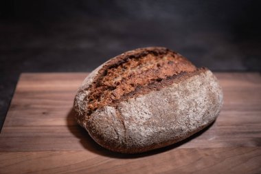 Ahşap tahtada yükselen kabuklu ev yapımı ekşi ekmeğin koyu arka planda yakın plan görüntüsü