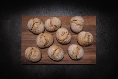 Kare tahta tahta üzerine yerleştirilmiş ev yapımı ekşi hamurdan ruloların yukarıdan aşağı stüdyo görüntüsü. Koyu tahta yüzeyine yerleştirilmiş.