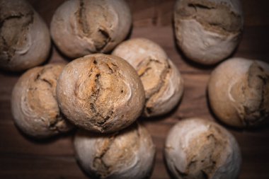 Yakın plan ahşap tahta üzerinde tek ekşi hamura odaklı, diğer rulo arka planda bulanık, ahşap yüzey altında görünür