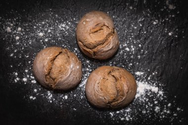 Üç ekşi ekmek rulosunun yakın plan görüntüsü. Koyu levha yüzeyine serpilmiş un serpiştirilmiş. Çerçeveyi dolduruyor.