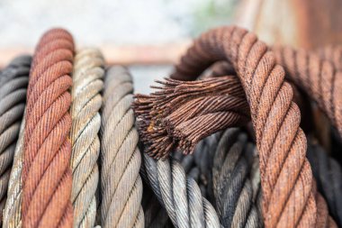 Değişen pas seviyeleri olan eski çelik kabloya yakın plan, hasarlı kablolar üzerine keskin odak, arkaplan kabloları giderek bulanıklaşıyor, eski endüstriyel dokuyu ve aşınmayı gösteriyor