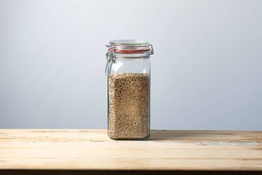 Çavdar taneleriyle dolu cam kavanoz rustik ahşap masa merkezli, yazı için kenarları boş, stüdyo ışıkları altında yakalanmış..