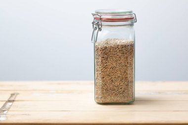 Çavdar taneleriyle dolu cam kavanoz, doğal mutfak ortamındaki sürdürülebilir tahıl deposunu gösteren yıllanmış ahşap masaya yerleştirilmiş..