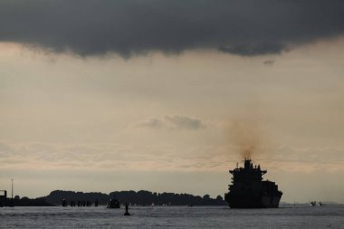 Akşam ışığı sırasında Elbe Nehri 'ndeki uzak gemi silueti, karanlık egzoz dumanları açıkça görülebiliyor duman yığınından sakin gökyüzüne yükseliyor, atmosferik sahne, Almanya' nın sessiz doğal arka planına karşı endüstriyel kirliliği gösteriyor