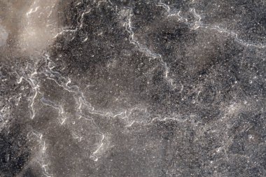 Kıyıdaki ince buz tabakasının makro yukarıdan aşağı görüntüsü. Dengesiz donmuş yüzeyde görünen hava kabarcığı izleri var. Kum ve taşlar şeffaf buzun altından belli belirsiz görünüyor.