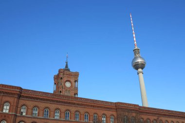 Berlin 'deki tarihi binanın ön cephesinin üst kısmında Berlin TV kulesi açık mavi gökyüzüne karşı görülebiliyor, öndeki eski yapı ile arkadaki modern kule arasındaki mimari karşıtlık
